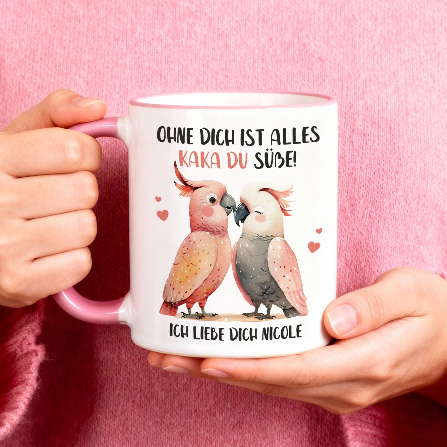 Personalisierte Tasse mit Kakadu-Pärchen und Spruch „Ohne dich ist alles Kaka du Süße!“ in der Hand gehalten, rosa Hintergrund