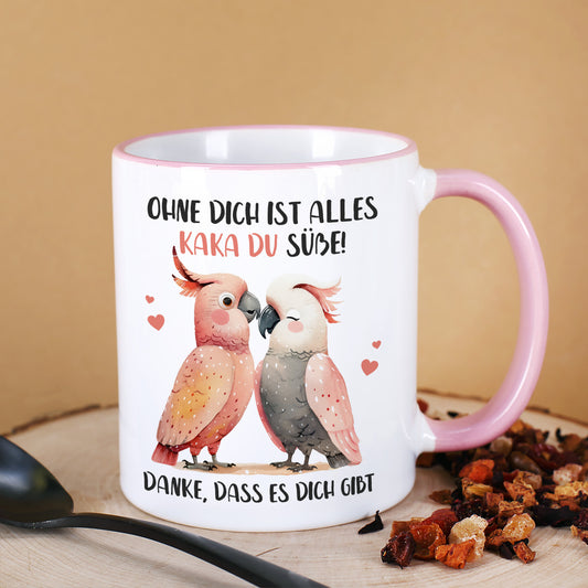 Kakadu-Tasse mit rosa Henkel und Wunschtext unter dem Motiv, dekoriert auf Holzscheibe mit Tee und Löffel