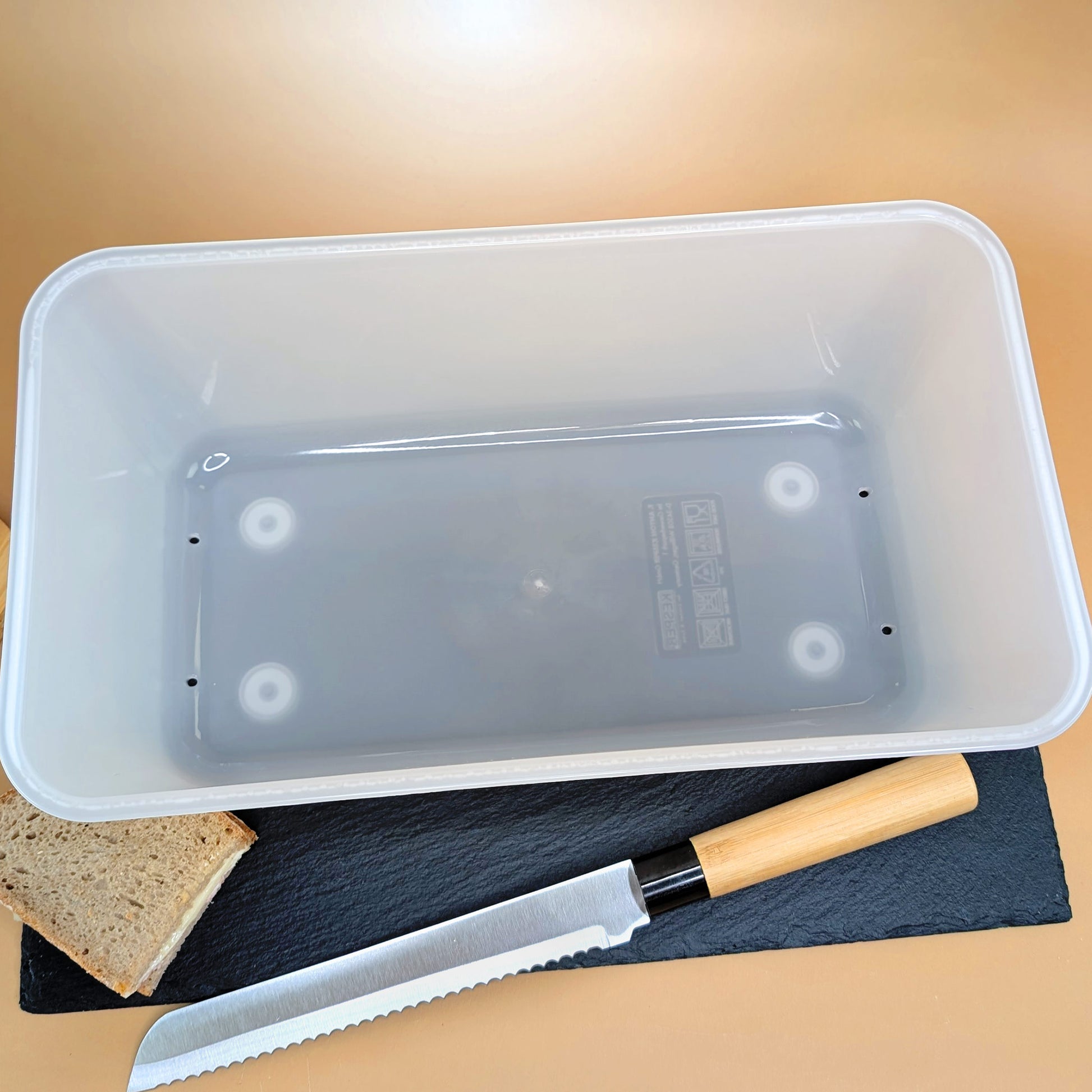 Blick von oben in die Brotbox, das Messer liegt daneben auf einer Schieferplatte.