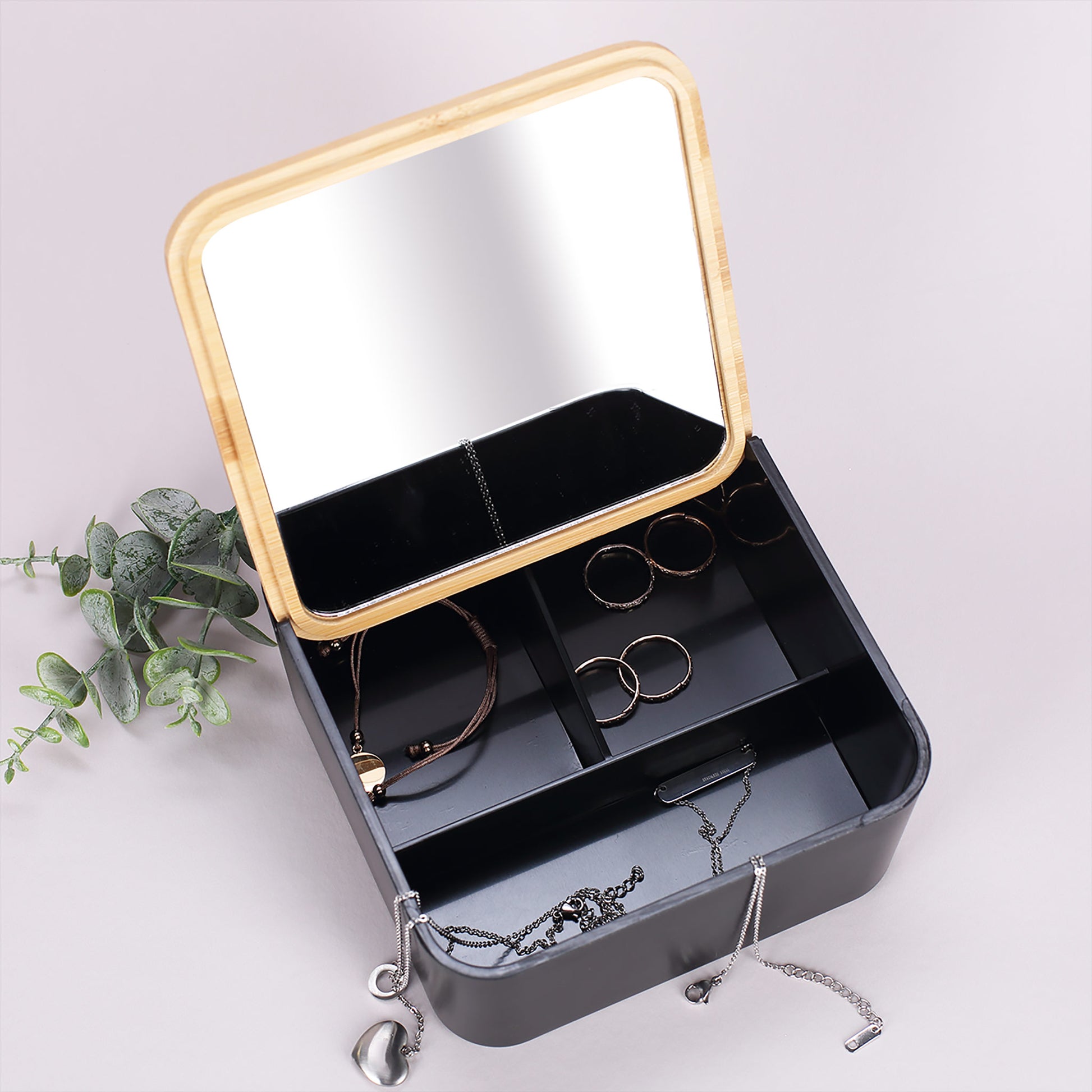 Schwarzer Schmuckkasten geöffnet, Bambusdeckel mit Spiegel sichtbar, Innenfächer erkennbar.
