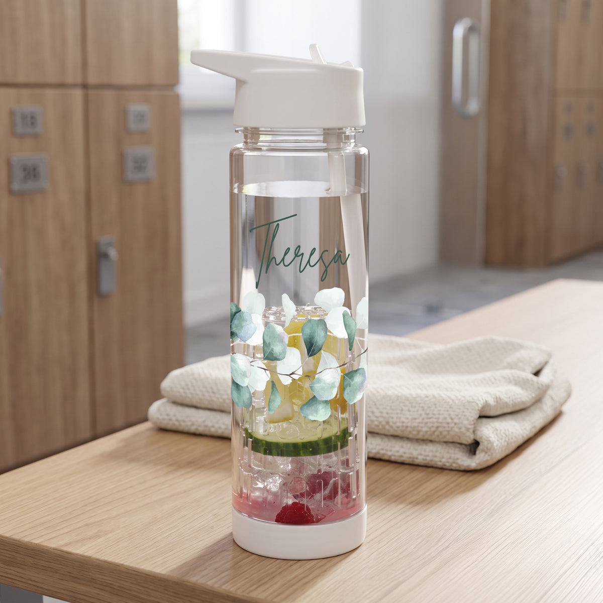 Personalisierte Trinkflasche mit Name Theresa, Eukalyptus-Motiv und Fruchteinsatz auf einer Holzbank im Umkleidebereich