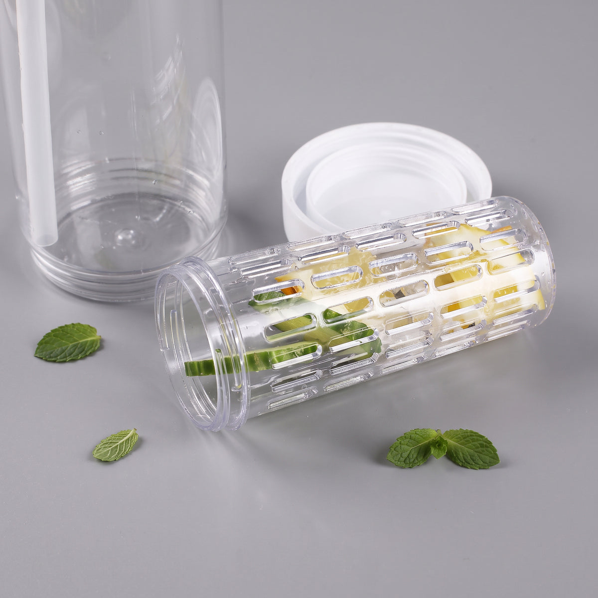 Herausnehmbarer Fruchteinsatz der Trinkflasche mit Zitronen- und Gurkenstücken neben Flasche und weißem Schraubring