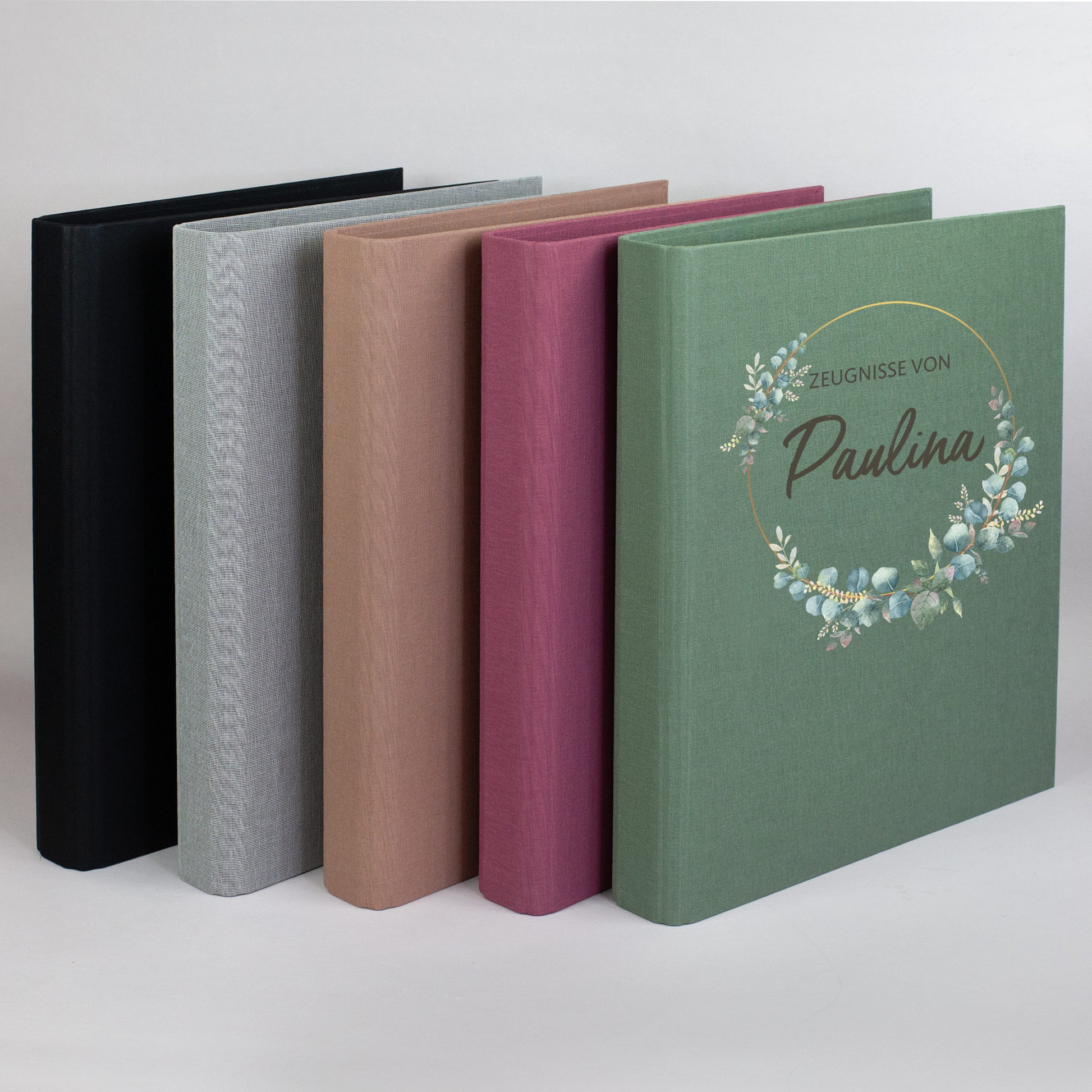 Zeugnismappen mit Eukalyptuskranz in allen Farben – braun, grau, grün, rosa und schwarz – nebeneinander aufgestellt