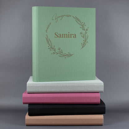 Zeugnismappe grün mit floralem Ring „meine Zeugnisse“ und Name Samira, personalisiert auf einem Stapel bunter Zeugnismappen