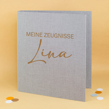 Zeugnismappe aus grauem Leinen mit Gravur „Meine Zeugnisse“ und personalisiertem Namen Lina.