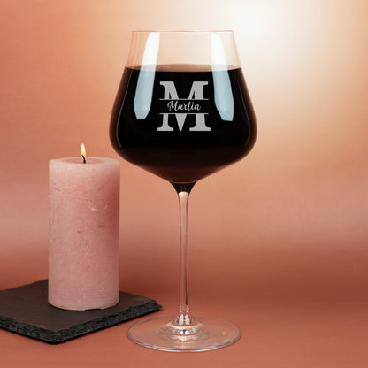 Graviertes Leonardo Burgunderglas mit Initiale M und Name Martin, daneben brennende rosa Kerze auf Schieferuntersetzer.