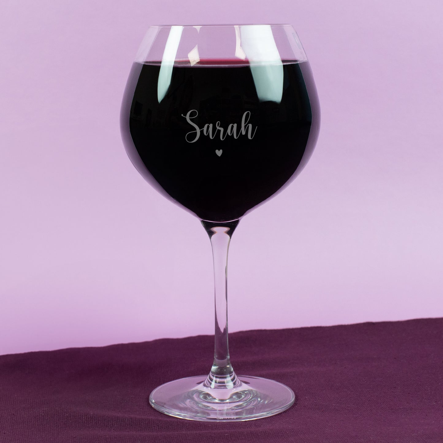 Personalisierte Gravur auf Leonardo Burgunderglas mit Name „Sarah“ und kleinem Herzmotiv – gefüllt mit Rotwein, vor pastellfarbenem Hintergrund, edel und romantisch gestaltet.