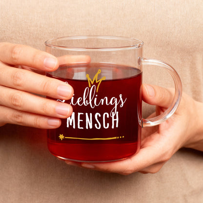 Leonardo-Teeglas mit Aufdruck „Lieblings Mensch“ in Weiß und Gold, gehalten in beiden Händen