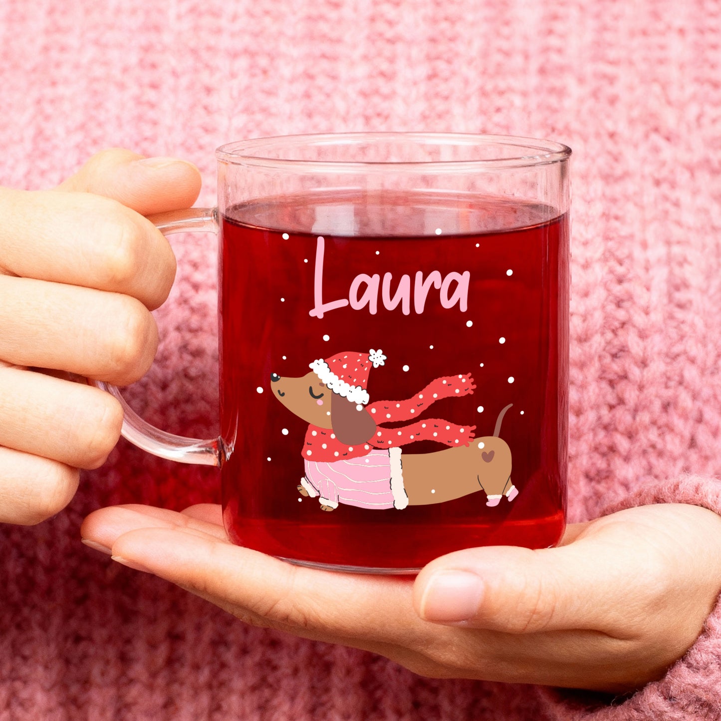 Teeglas mit personalisiertem Namen „Laura“ und winterlichem Dackelmotiv, gefüllt mit rotem Tee, in Händen gehalten