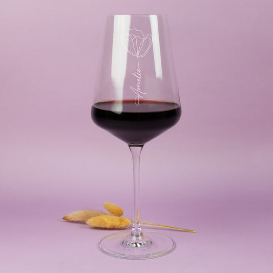 Elegantes Weinglas mit Gravur Name und Blumenmotiv mit Rotwein auf warmem Hintergrund
