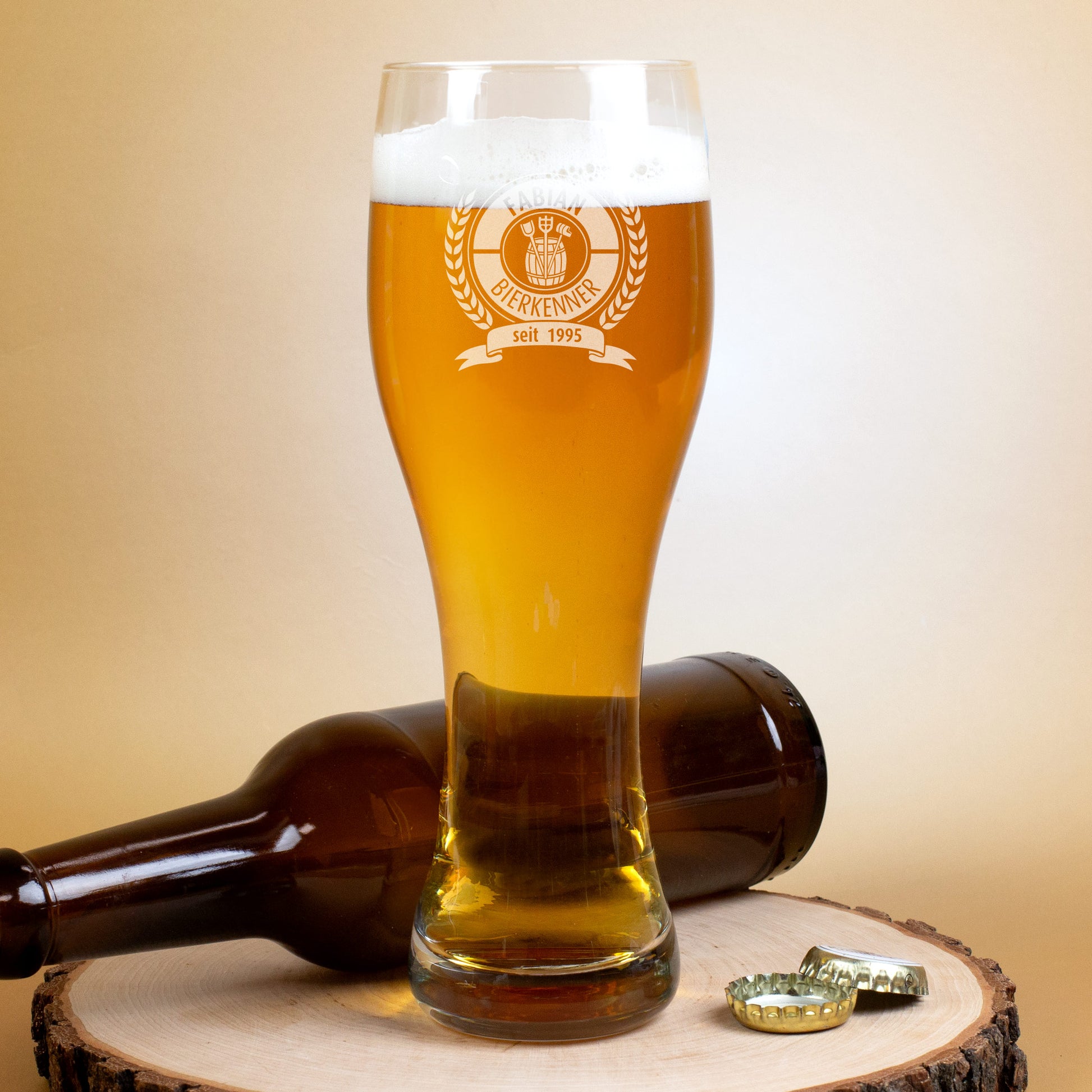 Personalisiertes Leonardo Weizenglas mit Gravur „Bierkenner“, gefüllt mit Bier auf Holzscheibe, daneben liegende Flasche
