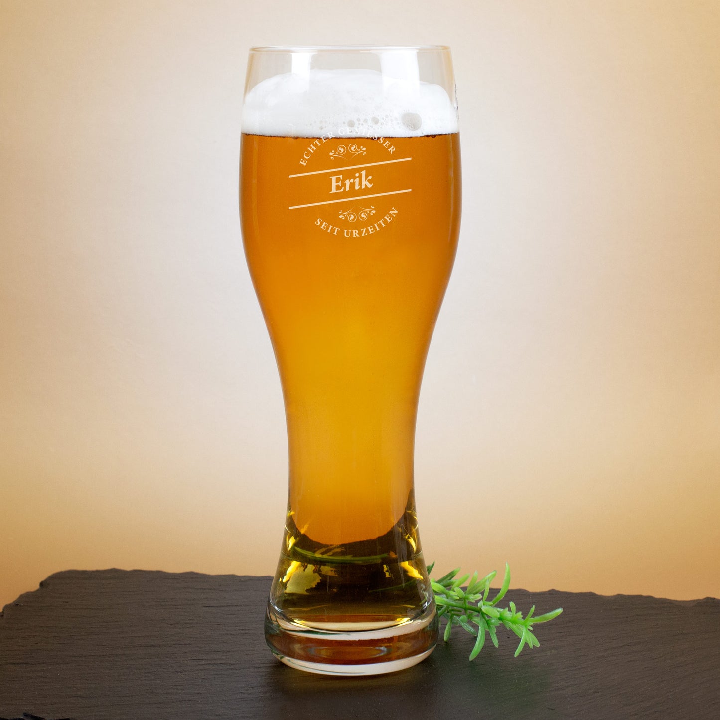 Graviertes Weizenglas mit Aufschrift „Echter Genießer seit Urzeiten“ und Name Erik, auf dunkler Unterlage mit Deko