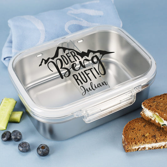 Personalisierte Brotdose aus Edelstahl mit Berg-Motiv und Name, auf Holzbrett mit Brot und Heidelbeeren