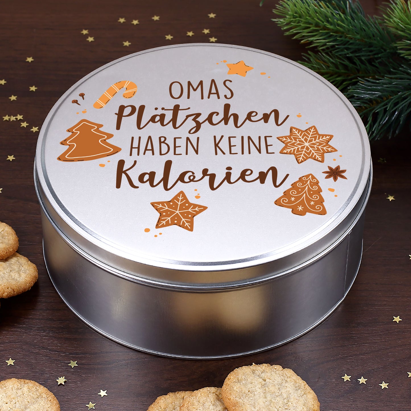 Runde silberne Blechdose mit Weihnachtsmotiv und Spruch „Plätzchen haben keine Kalorien“, dekoriert mit Tannenzweigen und Weihnachtsgebäck.