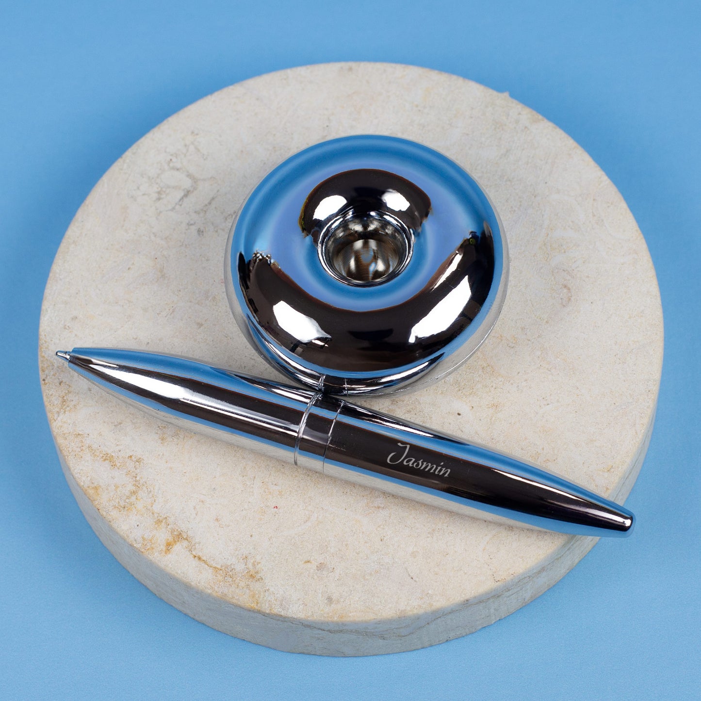 Magischer Kugelschreiber mit Namensgravur liegend neben Ständer auf blauem Hintergrund