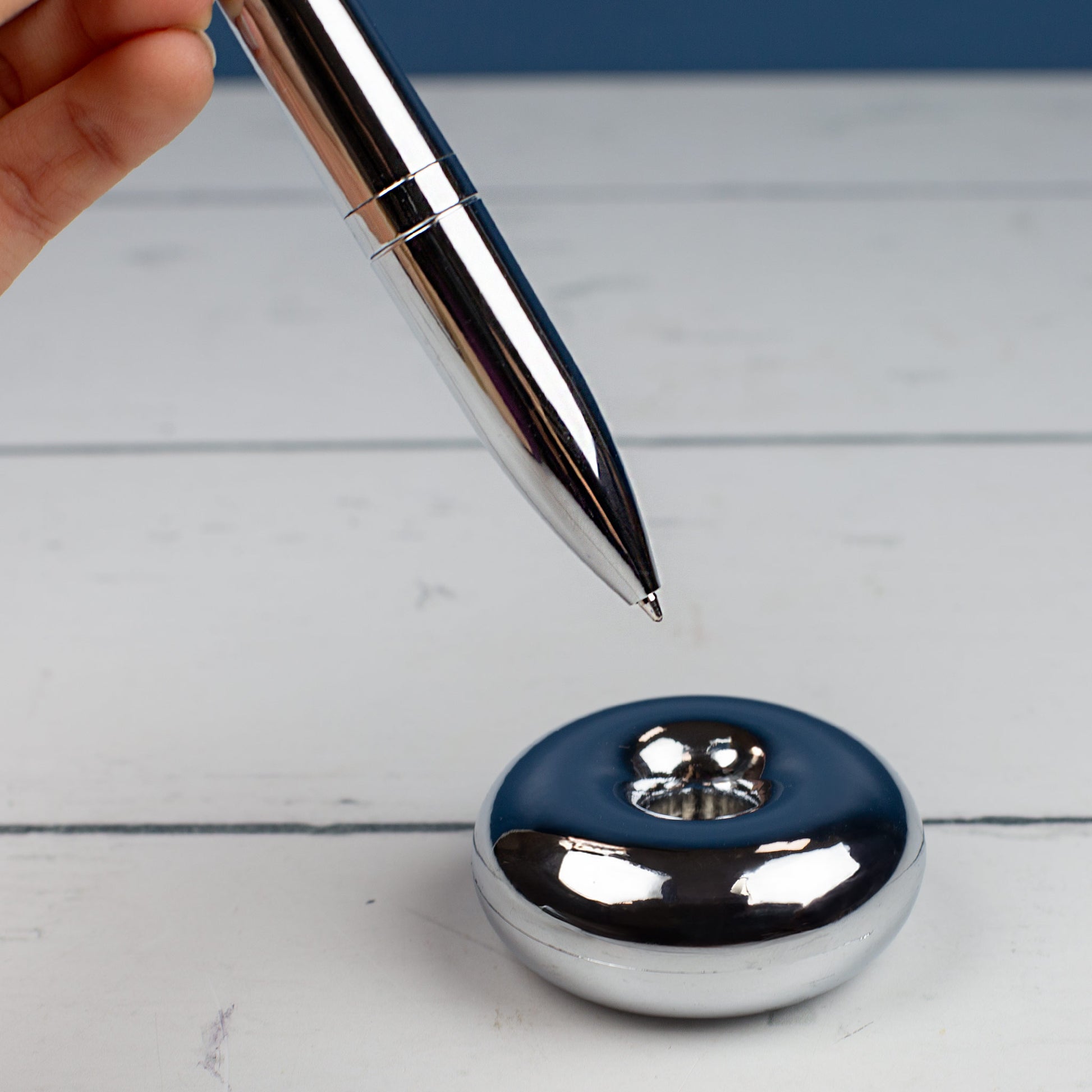 Magischer Kugelschreiber mit Namensgravur gehalten von einer Hand über Ständer