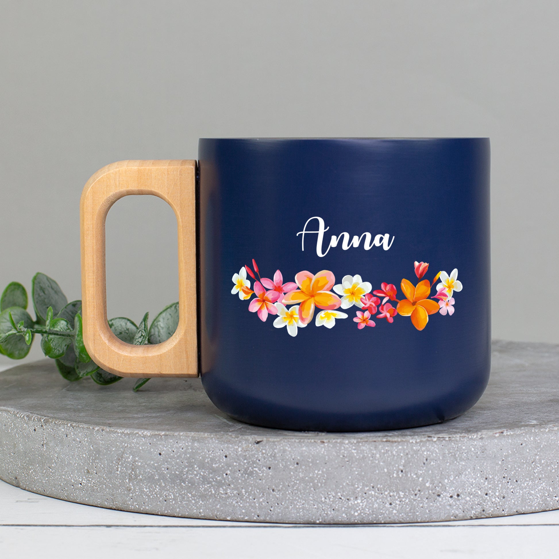 Personalisierter Edelstahlbecher mit Name Anna, bunten Blüten und natürlichem Holzgriff auf Betonplatte