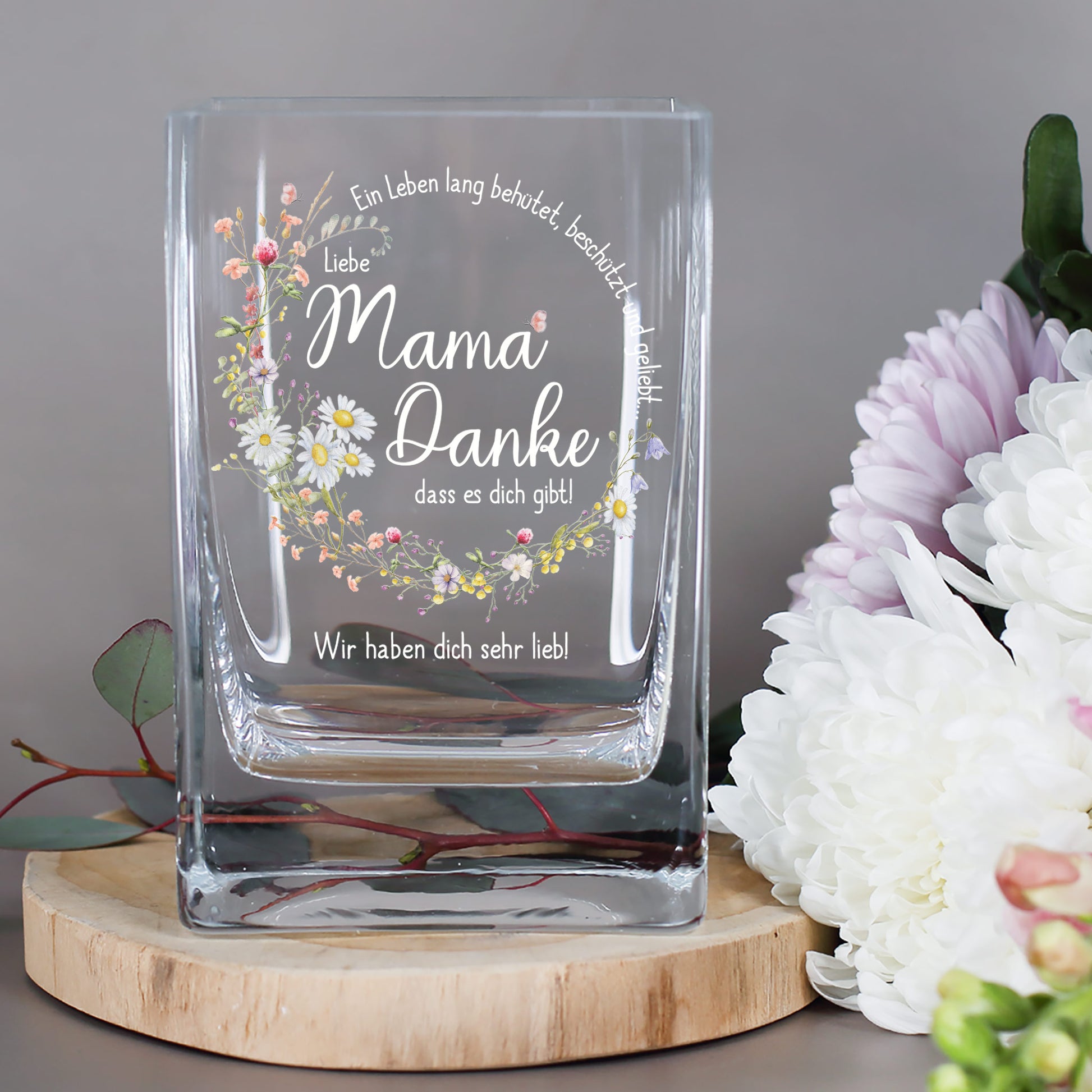 Glasvase mit floralem Druck und Spruch „Ein Leben lang behütet, beschützt und geliebt...“ daneben Chrysanthemen und Eukalyptus