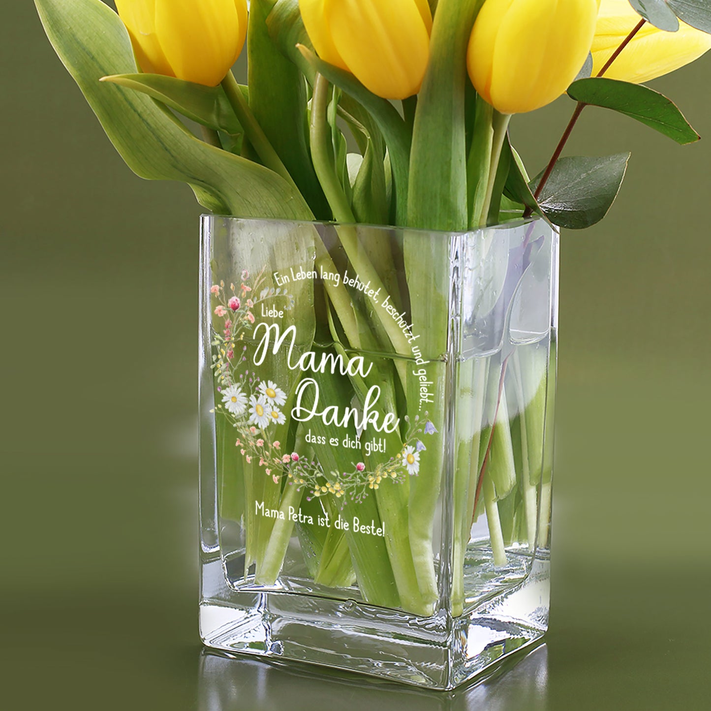 Gelbe Tulpen in personalisierter Vase mit Wiesenblumen-Kranz und dem Text „Mama Petra ist die Beste!“ auf grünem Hintergrund