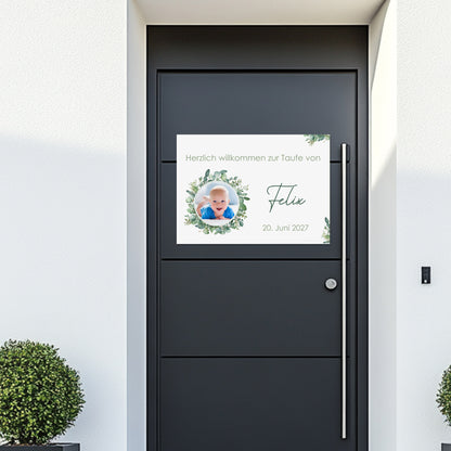Banner mit Babyfoto im Eukalyptuskranz an einer modernen Haustür. Text: „Herzlich willkommen zur Taufe von Felix – 20. Juni 2027“. Schlichte, elegante Gestaltung mit Namen und Datum.
