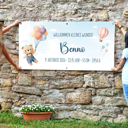 XXL Baby Banner für Jungen mit Name Benno und Wunschtext „Willkommen kleines Wunder“, befestigt an einer Steinwand im Außenbereich
