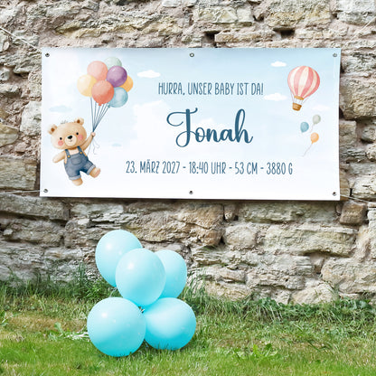 Personalisiertes Geburtsbanner mit Teddy Motiv, Name Jonah, Geburtsdatum, Uhrzeit, Größe und Gewicht an Steinwand mit blauen Ballons
