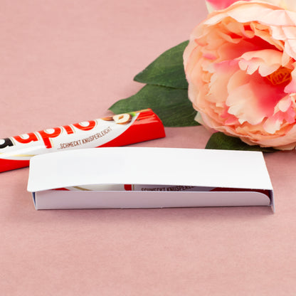 Geöffnete Geschenkverpackung für duplo Riegel mit weißer Innenlasche, Schokoriegel und dekorativer Blume