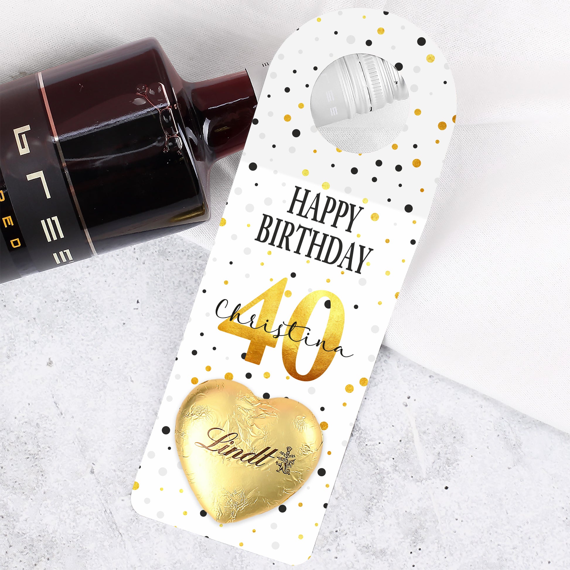 Nahaufnahme des großen Geburtstags-Flaschenanhängers mit personalisiertem Namen, Alter und aufgeklebtem Lindt-Schokoladenherz.