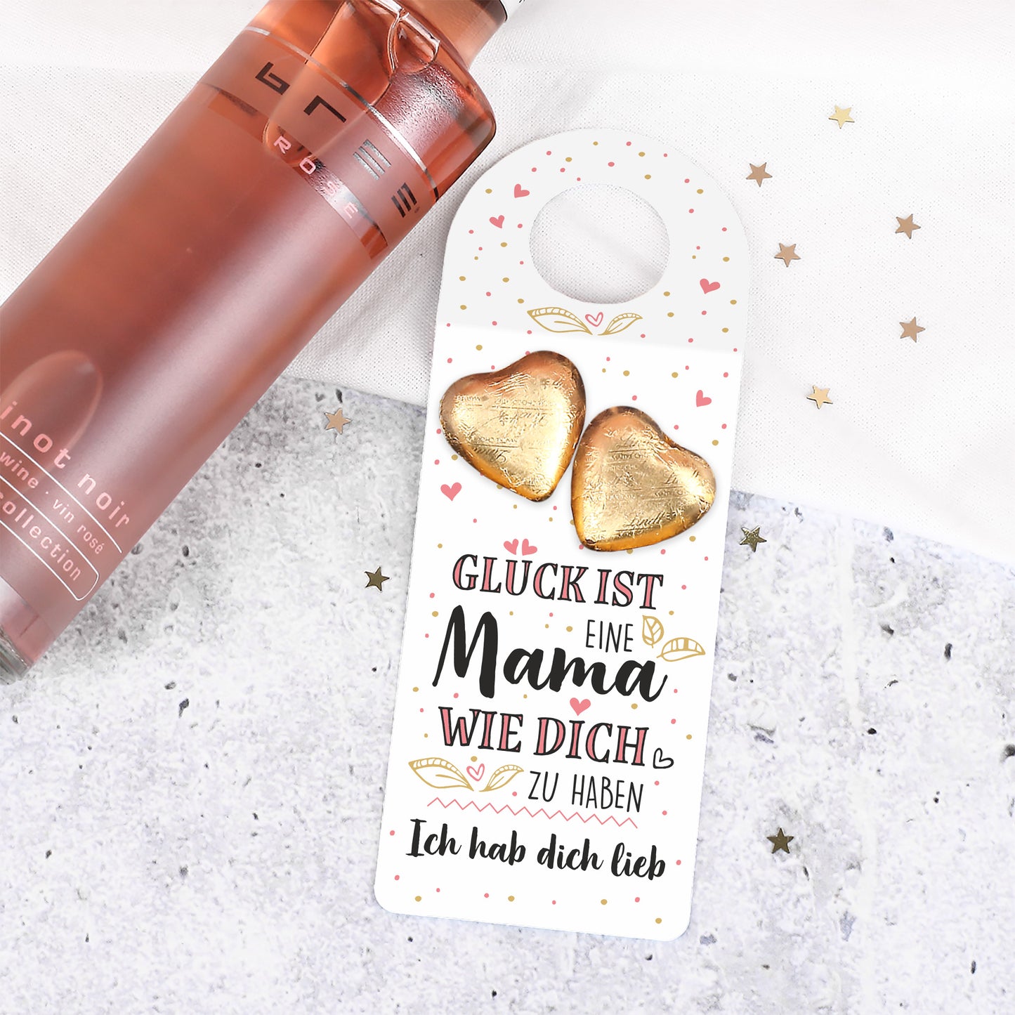 Roséweinflasche mit Flaschenanhänger zum Muttertag und zwei Schokoherzen auf hellem Untergrund
