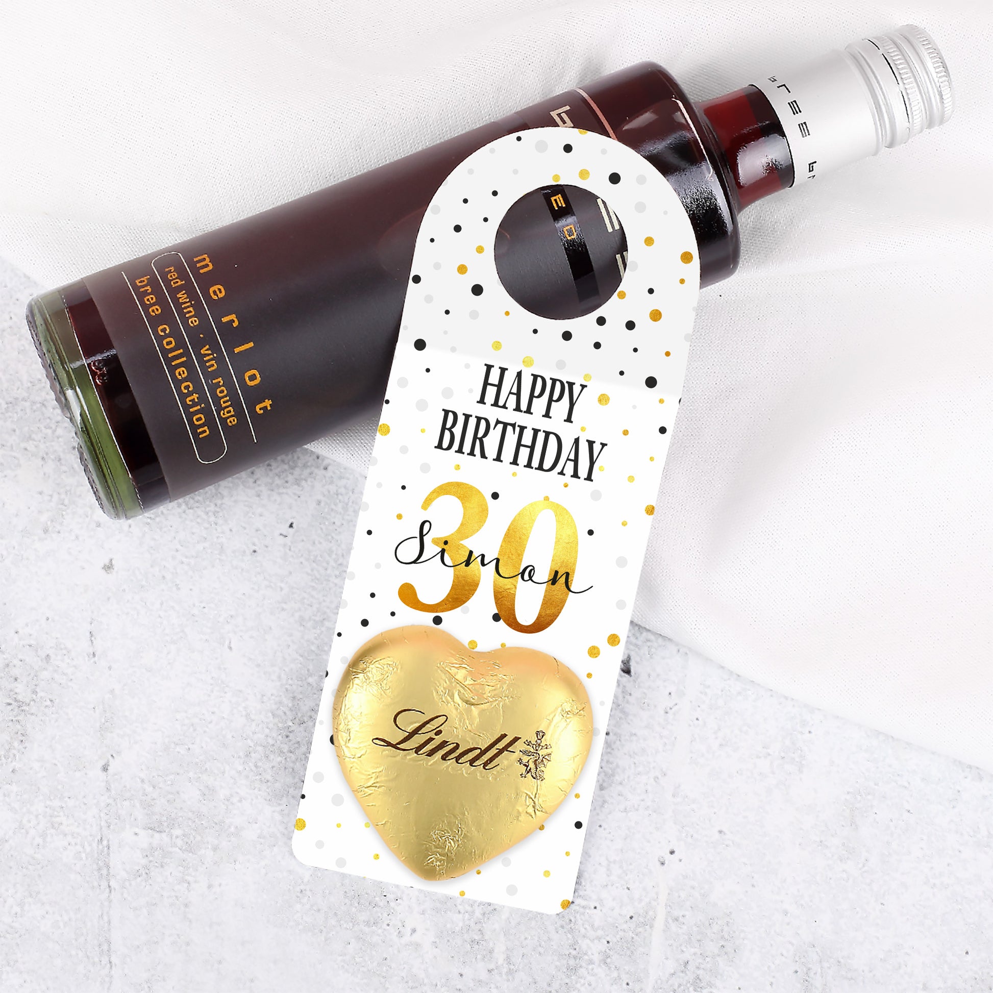 Nahaufnahme des kleinen Geburtstags-Flaschenanhängers mit personalisiertem Namen, Alter und aufgeklebtem Lindt-Schokoladenherz.