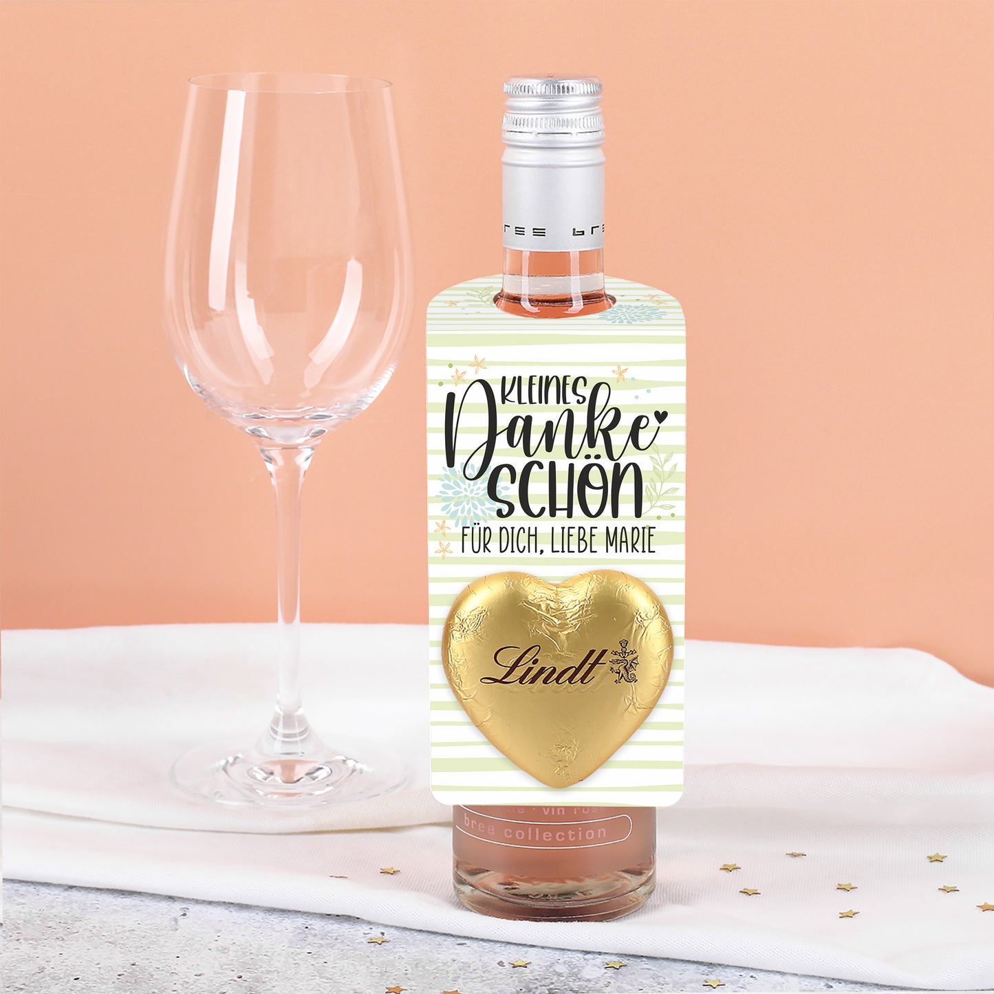 Kleiner Flaschenanhänger in Hellgrün mit Aufdruck „Kleines Dankeschön“, Lindt Schokoladenherz und personalisiertem Text an einer Flasche befestigt.