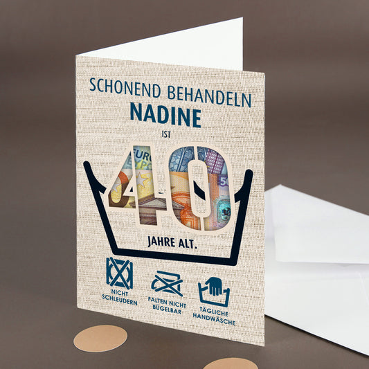 Klappkarte „Schonend behandeln – Nadine ist 40 Jahre alt“ mit Geldschein im Ausschnitt und Umschlag im Hintergrund