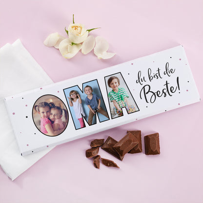 Personalisierbare Fotogeschenk-Schokolade „Oma“ mit 3 Bildern und Schokoladenstücken auf rosa Untergrund mit Blume