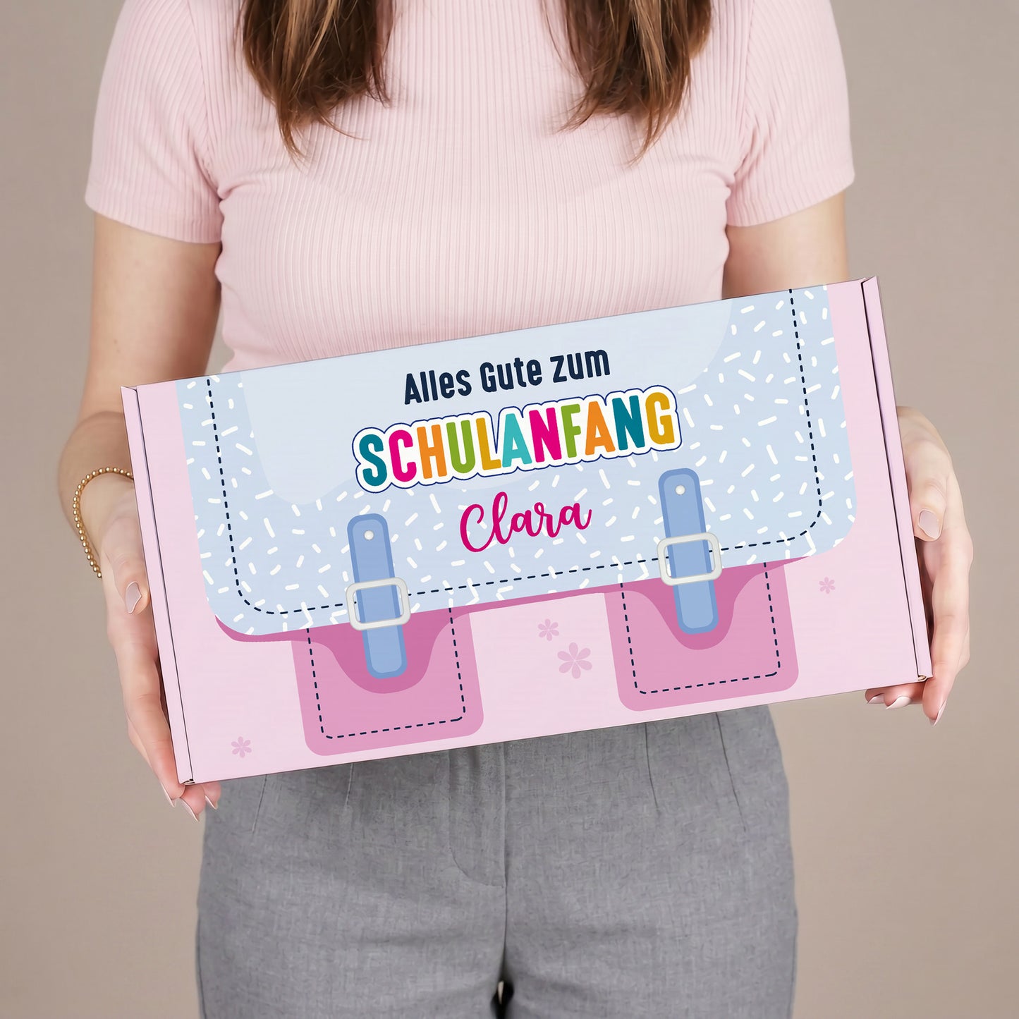 Mittlere rosa Geschenkverpackung zum Schulanfang mit Name und Schulranzen-Design, von einer Person gehalten