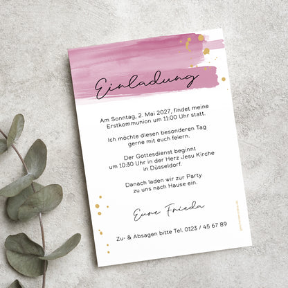 Einladungskarte zur Erstkommunion mit modernem Aquarell-Design in Rosa und goldenen Akzenten. Die Karte ist mit individuellem Einladungstext personalisiert und liegt auf einer Naturstein-Oberfläche, umgeben von Eukalyptusblättern.