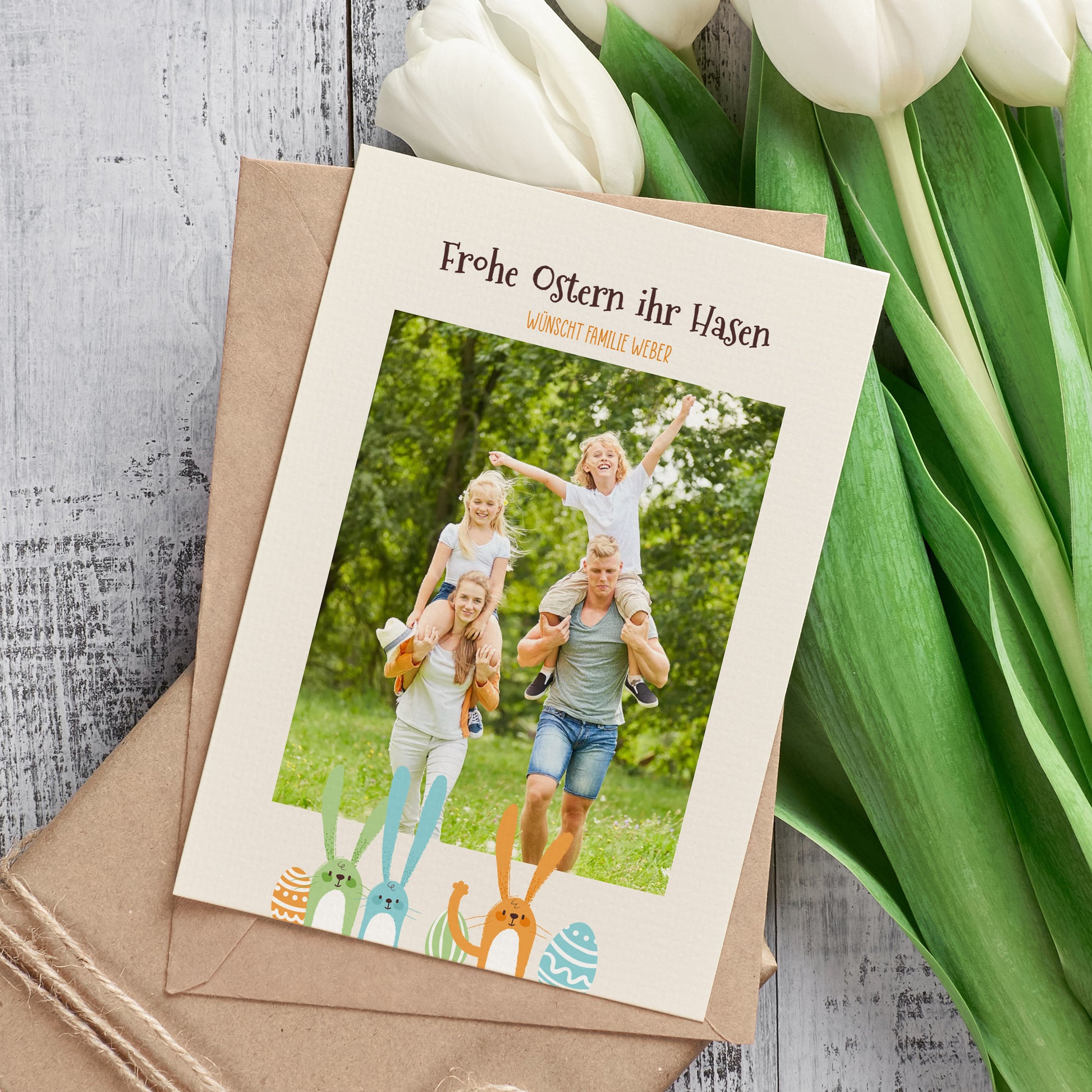 Personalisierte Osterkarte mit Foto und Hasenmotiv sowie Umschlag neben Tulpen dekoriert