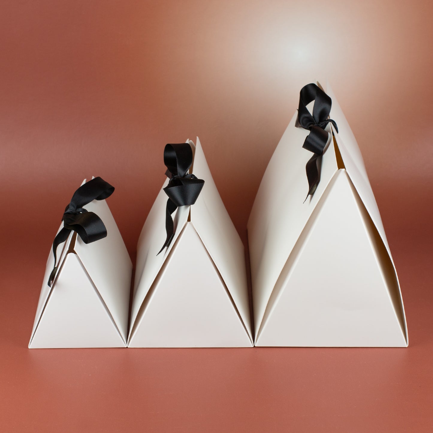 Seitenansicht der Geschenkverpackungen in drei Größen – weiße Faltverpackung mit schwarzer Schleife