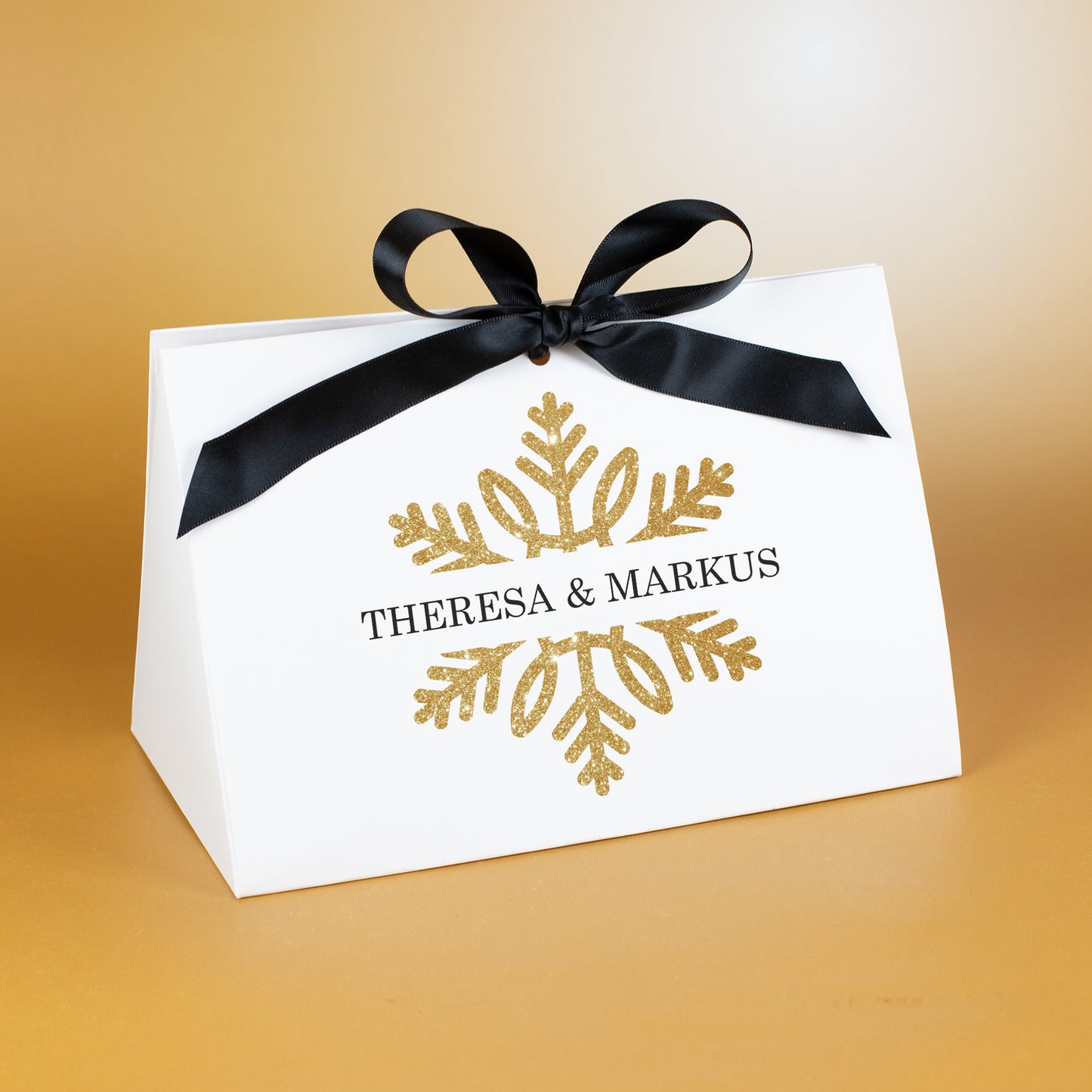 Große Geschenktasche mit goldfarbener Schneeflocke und personalisierter Aufschrift „Theresa & Markus“, edel vor warmem Hintergrund platziert.