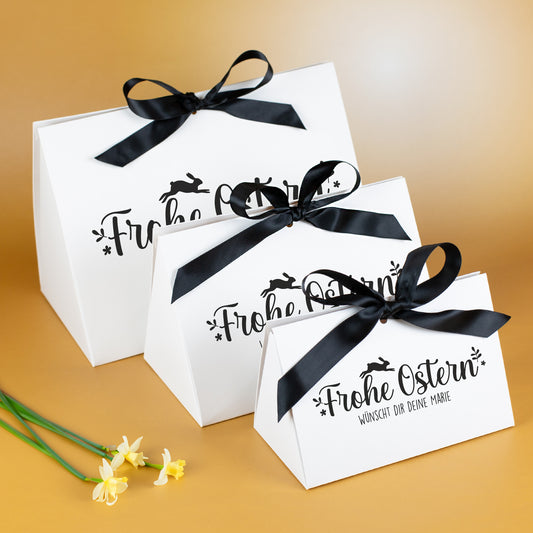 Drei weiße Oster-Geschenkverpackungen mit schwarzer Schleife und Frohe Ostern Motiv
