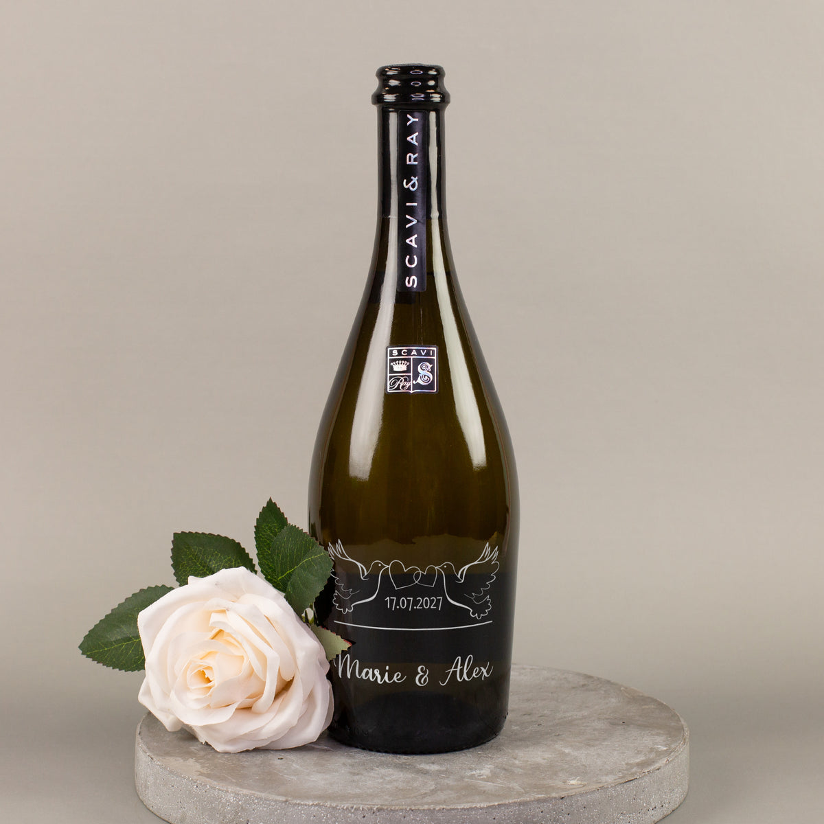 Personalisierte Scavi & Ray Prosecco-Flasche zur Hochzeit mit Datum und Namen Marie & Alex neben weißer Rose