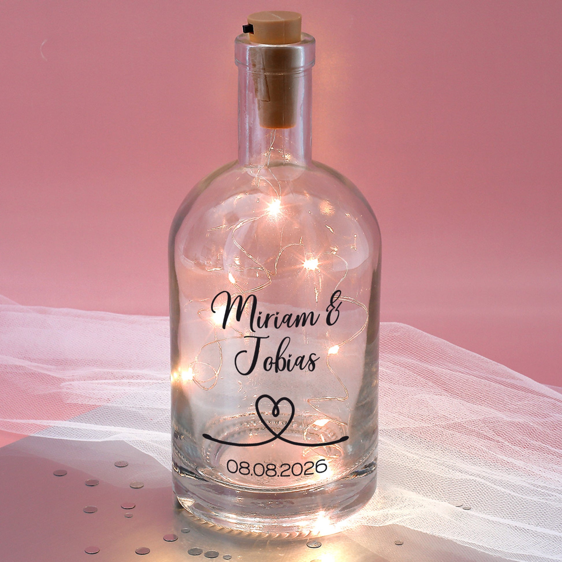 Bedruckte Glaskaraffe mit LED-Lichterkette vor rosa Hintergrund