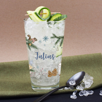 Nahaufnahme eines personalisierten Glases mit Tannenzweigen und Eichhörnchen-Motiv, dekoriert mit Gurken und Eiswürfeln
