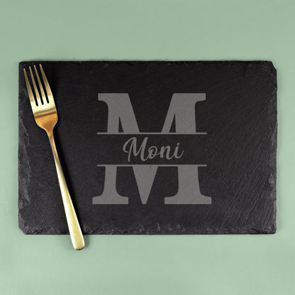 Schieferplatte mit Gravur „M“ und Name Moni, rechteckige Servierplatte mit goldener Gabel auf grünem Hintergrund