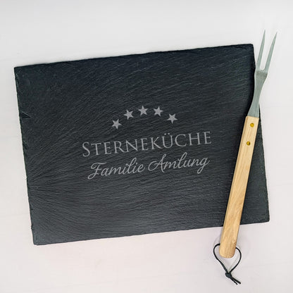 Schieferplatte mit Gravur „STERNEKÜCHE Familie Amlung“, seitlich dekoriert mit Grillgabel – fotografiert auf hellem Untergrund