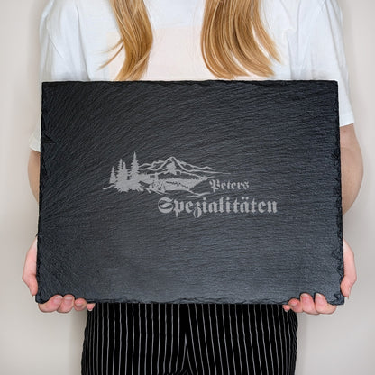 Rechteckige Schieferplatte mit Gravur „Peters Spezialitäten“, gehalten von einer Person in weißem Shirt