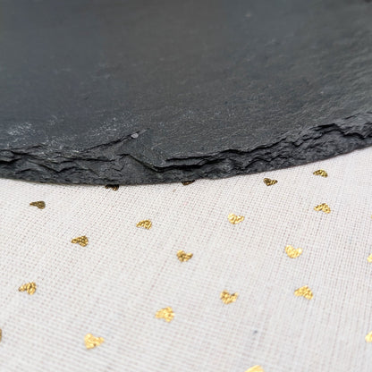 Nahaufnahme der natürlichen Bruchkante der Schieferplatte auf weißem Tuch mit Goldpunkten