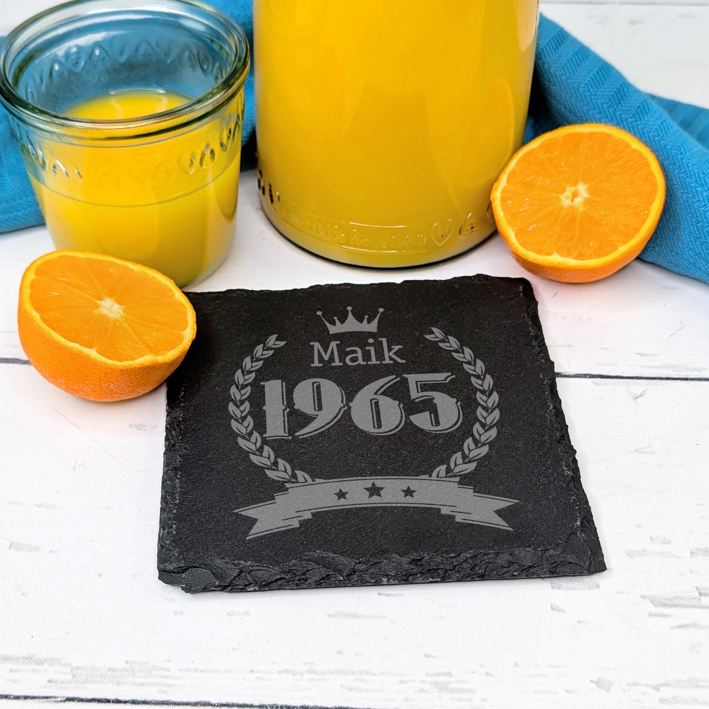 Schiefer-Untersetzer mit Krone und Geburtsjahr 1965, Name Maik, auf Frühstückstisch mit Orangen