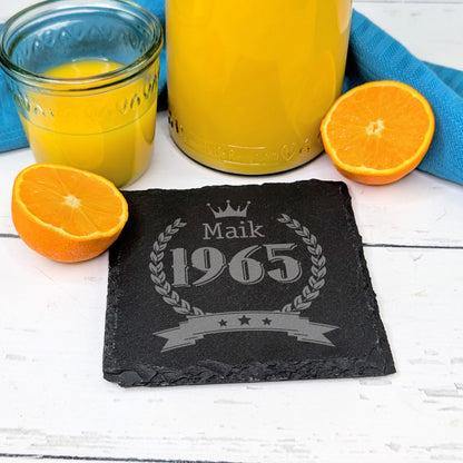 Schiefer-Untersetzer mit Krone und Geburtsjahr 1965, Name Maik, auf Frühstückstisch mit Orangen