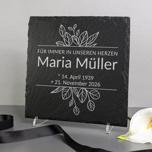 Gedenktafel auf einem Ständer dekoriert – neben Blume und Trauerband platziert