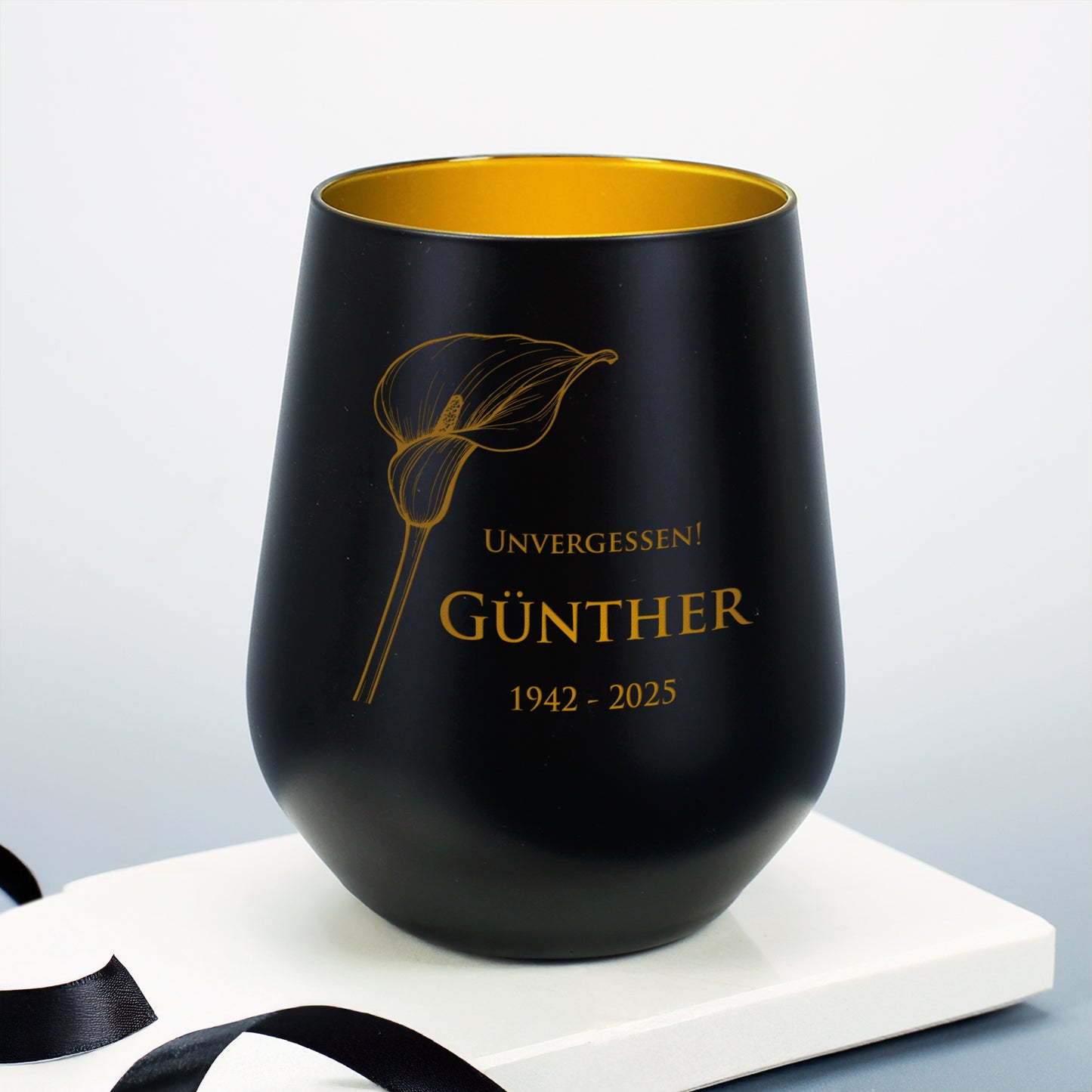 Schwarzes Windlicht mit Calla-Motiv, graviert mit "Unvergessen! Günther 1942–2025", auf weißem Sockel mit Schleifenband
